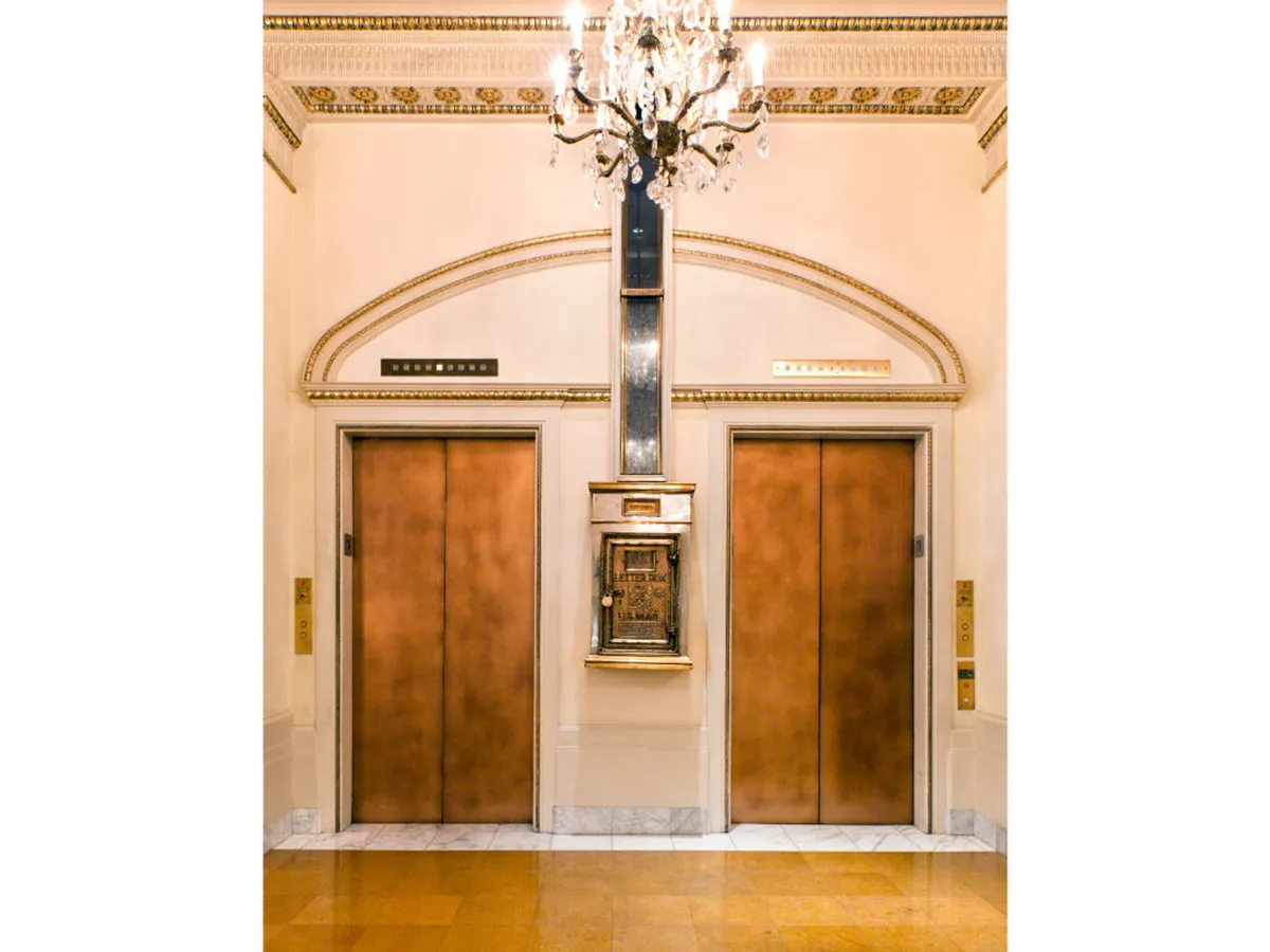 An ornate hotel lobby scene showcasing elegant elevator doors, a sparkling chandelier overhead, and intricate wall detailing. The space exudes a sense of arrival and luxury, hinting at the experience guests have when setting out or returning from city escapades.