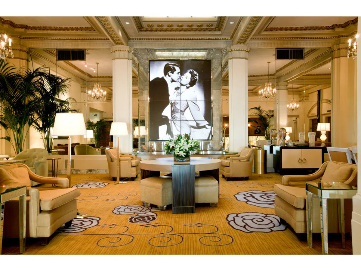 A sophisticated common area features a central table adorned with a fresh floral arrangement, eye-catching black-and-white artwork, and sparkling chandeliers. The mood is refined yet comfortable, offering space for relaxation or social gatherings.