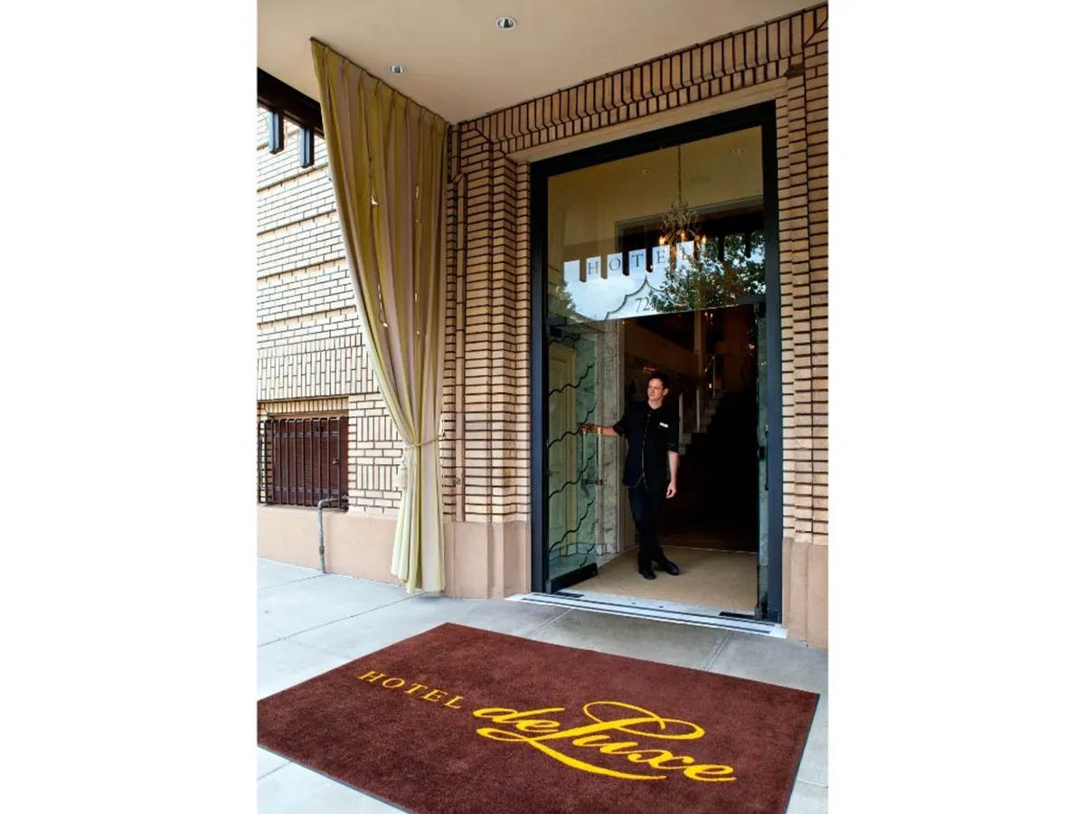 The hotel’s exterior entrance with a visible hotel mat and a friendly staff member greeting guests, suggesting a warm and welcoming arrival experience.