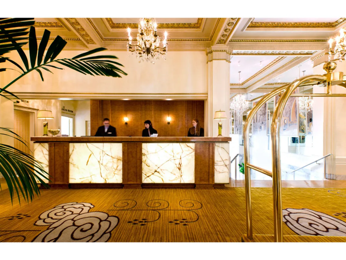 This image captures the lobby’s reception desk, where staff members interact warmly with guests beneath an elegant chandelier. Lush greenery and stylish decor set the tone for a welcoming environment. The overall mood is elegant and professional, showcasing attentive service and a seamless check-in process.
