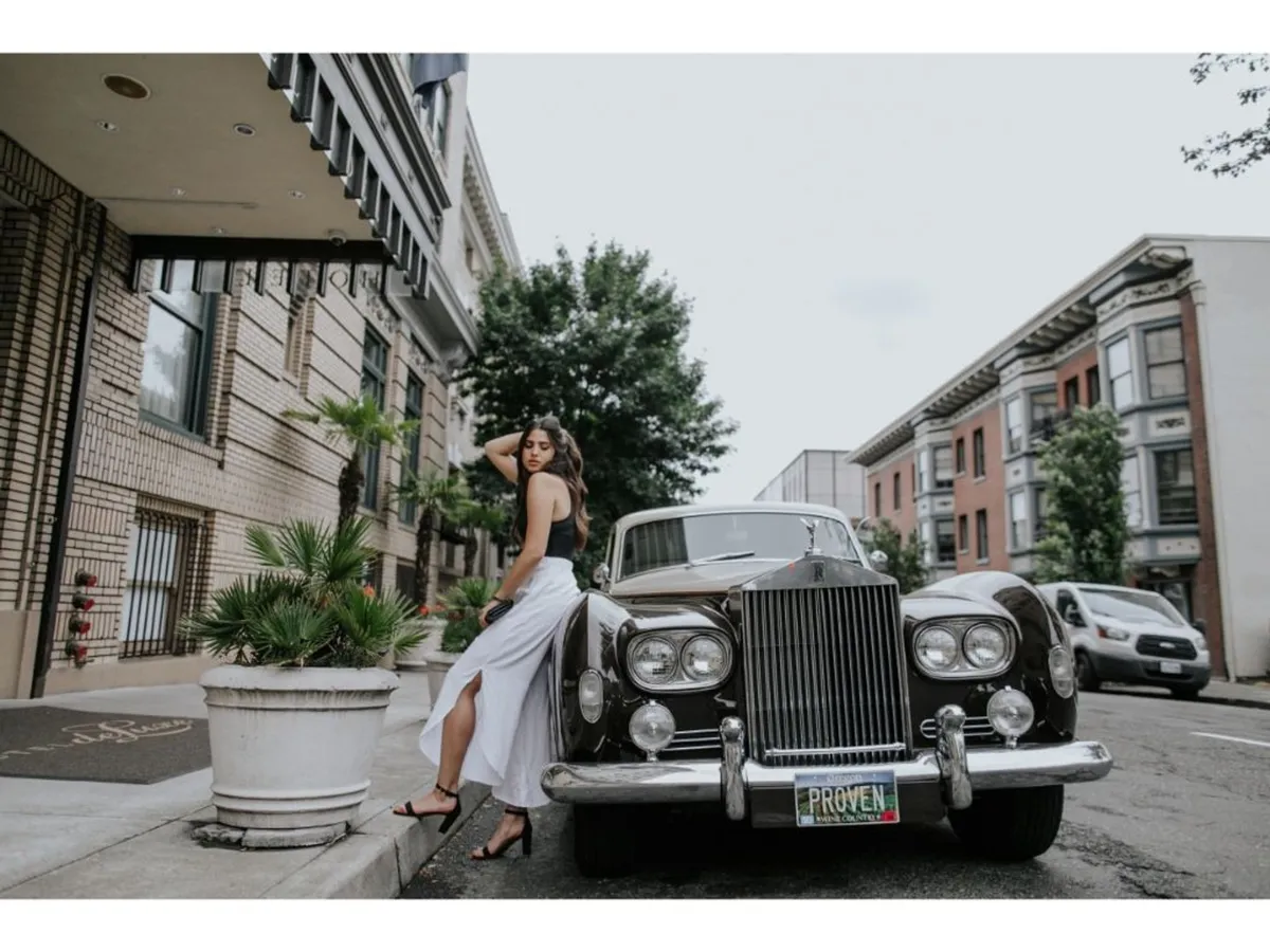 An exterior street scene featuring a classic car and a model posing, set against the backdrop of elegant urban architecture. This vibrant, stylish moment captures the spirit of exploring the neighborhood, with hints of vintage sophistication and opportunities for memorable photos.