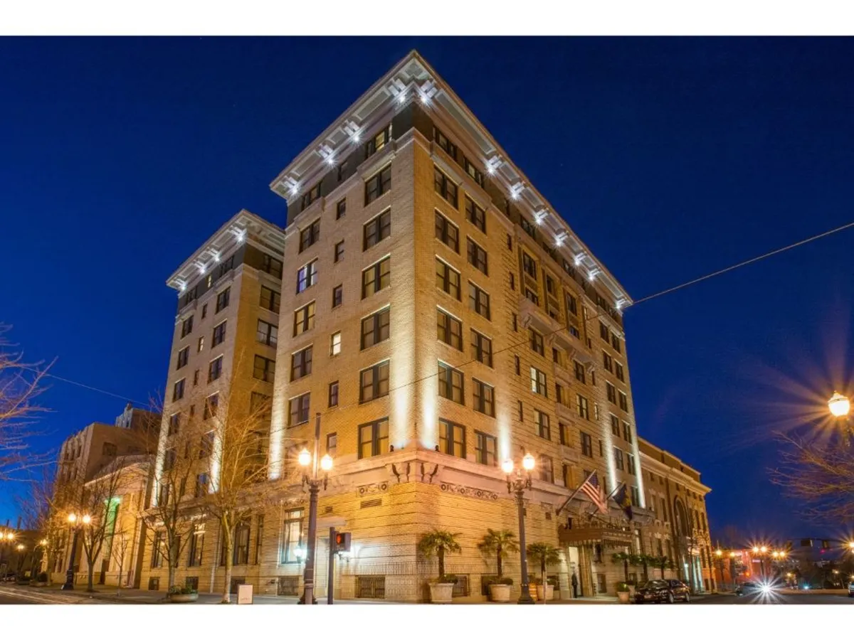 A beautifully illuminated hotel façade at dusk, with visible streetlamps, landscaping, and the inviting architectural details of the building. The scene hints at proximity to urban activity and nearby amenities.